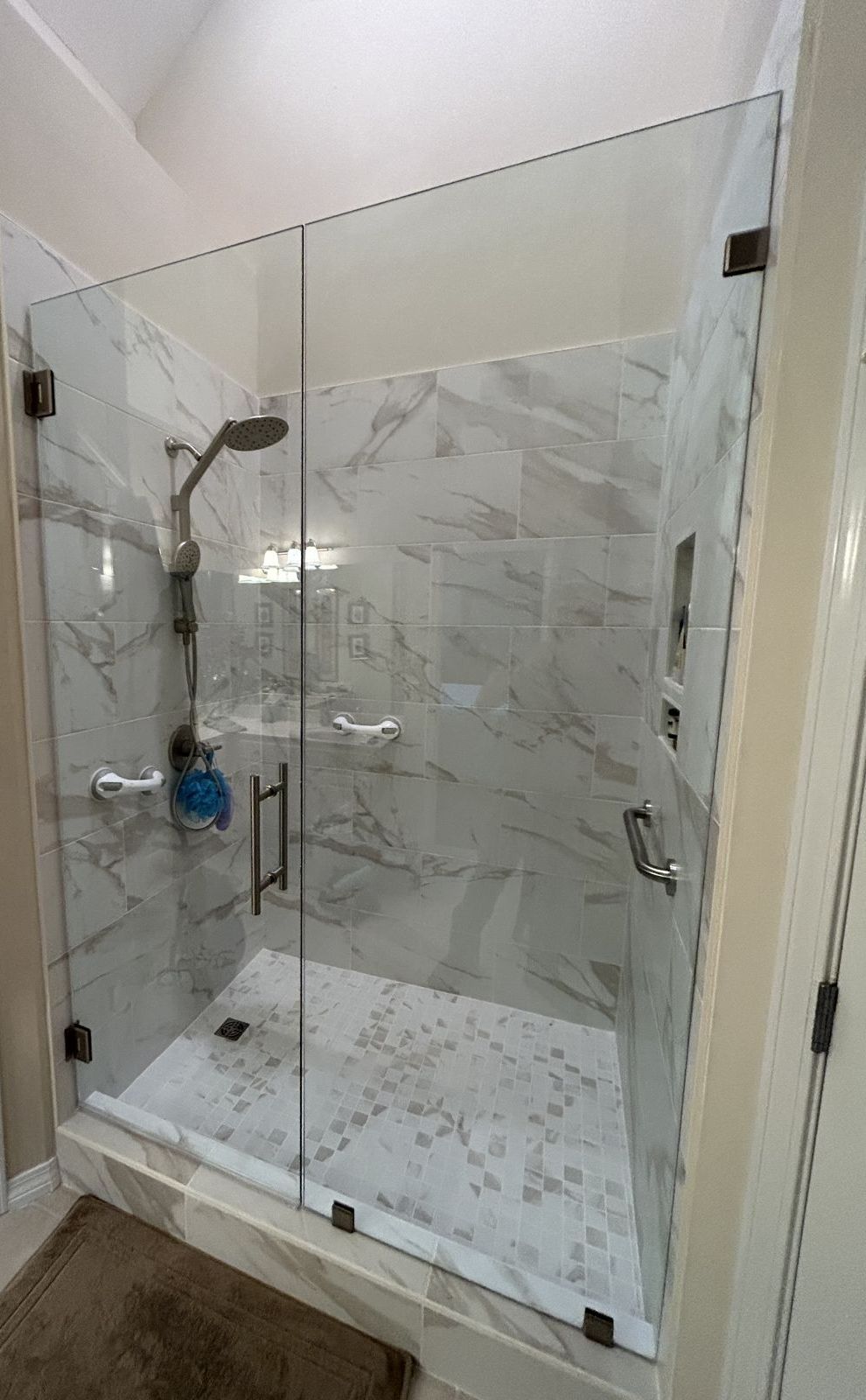 Angled view of a frameless glass shower door and panel with brushed nickel hardware