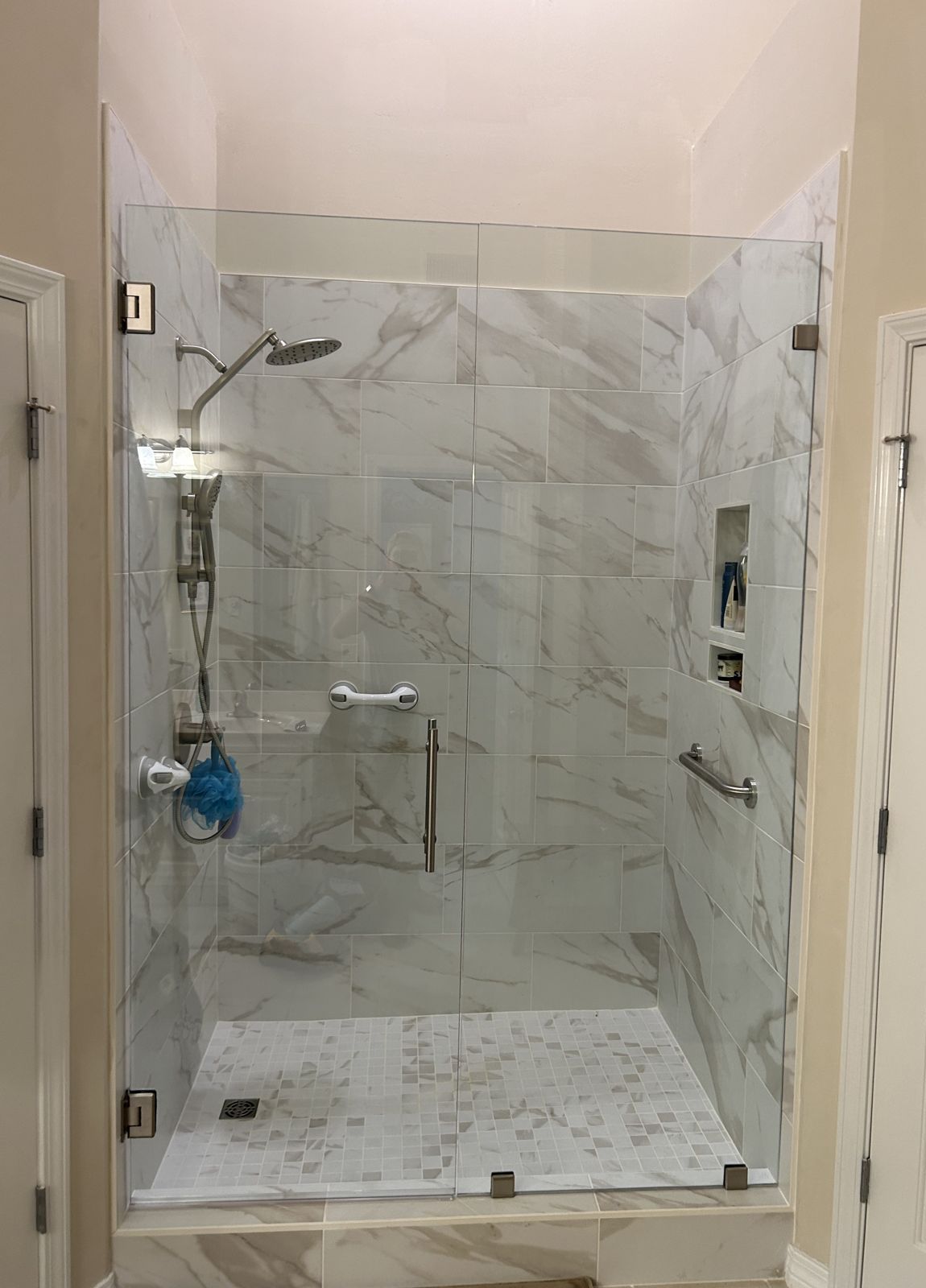 Frameless glass shower enclosure with a hinged door and fixed panel, marble-look tile